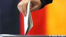 Человек бросает бюллетень в избирательную урну на фоне флага Германии