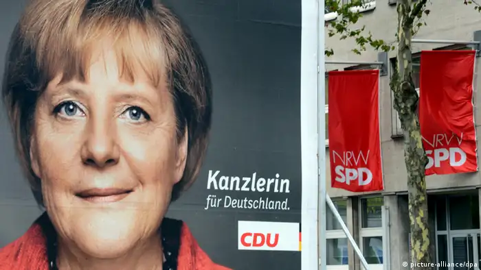 Ein Wahlplakat der CDU für die Bundestagswahl am 22.September mit einem Portrait der Bundeskanzlerin Merkel steht am 20.09.2013 in Düsseldorf (Nordrhein-Westfalen) vor dem mit Fahnen geschmückten Gebäude der Geschäftsstelle des Landesverbandes der SPD Nordrhein-Westfalen. Foto: Horst Ossinger/dpa