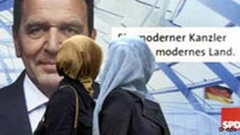 Archivbild: Zwei Türkinnen laufen vor einem Wahlplakat, auf dem Gerhard Schröder abgebildet ist, her und schauen sich zu diesem um (Foto: dpa)