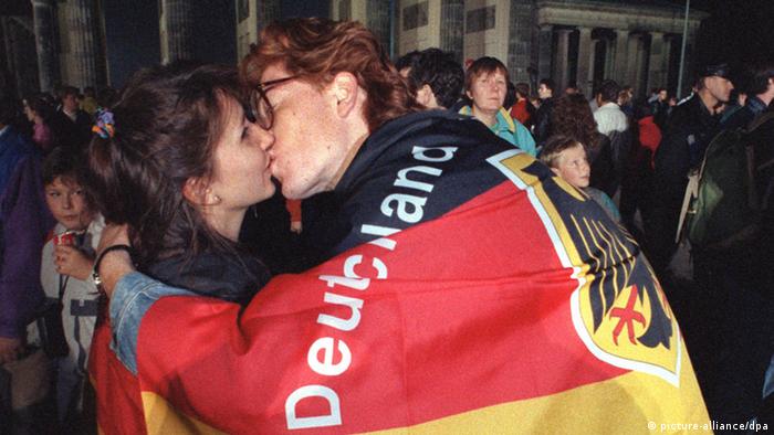 Покрытый флагом Германии молодой человек целует девушку у Бранденбургских ворот в Берлине