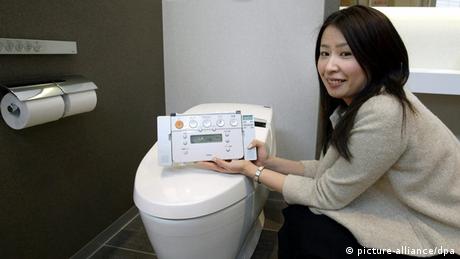 Awoman crouches next to a toilet, showing a tablet 