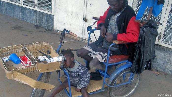 Ein Mann sitzt auf einem Fahrrad, das zum Rollstuhl umgebaut worden ist. In zwei Körben liegen Zigarettenpackungen. Seine Tochter sitzt ebenfalls auf dem Rad. 
