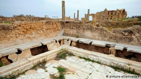 Ancient Roman toilets, marble ledges, excavations and ruins in the background 