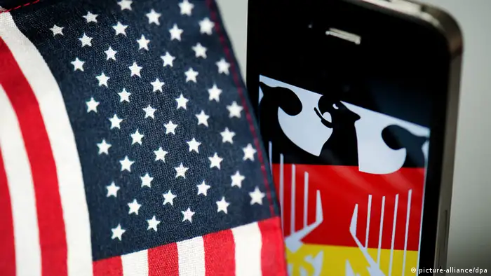ILLUSTRATION - Ein iPhone, auf dem der Bundesadler zu sehen ist, steht am 25.10.2013 in Dresden (Sachsen) neben einer US-Fahne. Nach Hinweisen auf eine Überwachung des Handys von Bundeskanzlerin Merkel (CDU) durch US-Geheimdienste haben Politiker aller Parteien umgehende Aufklärung gefordert. Foto: Arno Burgi/dpa