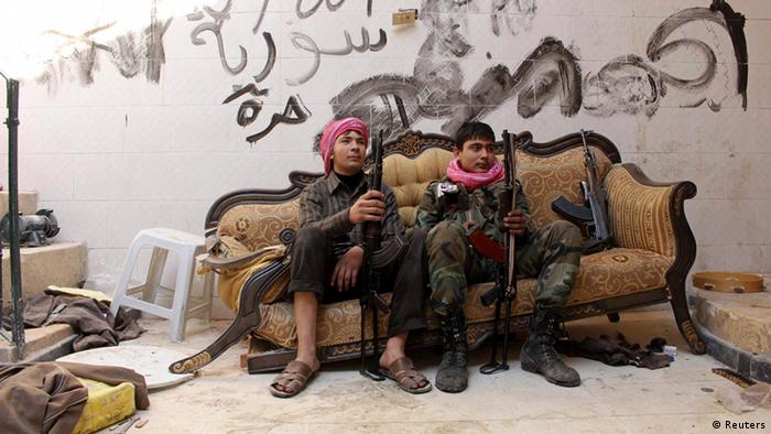 Zwei Jungen, die für die Freie Syrische Armee kämpfen, posieren auf einer kaputten Couch in einem Haus. An der Wand die Aufschrift: Gott, Syrien, Frei. (Foto: REUTERS/Molhem Barakat)
