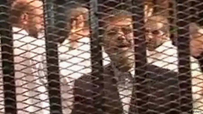 Ousted former Egyptian President Mohamed Mursi stands in a cage in a courthouse on the first day of his trial, in Cairo, in this still image taken from video provided by Egypt's Interior Ministry on November 4, 2013. Defendants in his trial, dressed in white, make the four-fingered Raba'a sign in solidarity with the Muslim Brotherhood behind Mursi. Egyptian state television on Monday aired footage of Mursi in a cage in a Cairo courthouse where he was on trial on charges of inciting violence. It was the first public sighting of Mursi since he was ousted by the army on July 3 after mass protests against his rule. REUTERS/Egypt Interior Ministry/Handout via Reuters (EGYPT - Tags: POLITICS CRIME LAW TPX IMAGES OF THE DAY) ATTENTION EDITORS - THIS IMAGE HAS BEEN SUPPLIED BY A THIRD PARTY. IT IS DISTRIBUTED, EXACTLY AS RECEIVED BY REUTERS, AS A SERVICE TO CLIENTS. NO SALES. NO ARCHIVES. FOR EDITORIAL USE ONLY. NOT FOR SALE FOR MARKETING OR ADVERTISING CAMPAIGNS. MANDATORY CREDIT