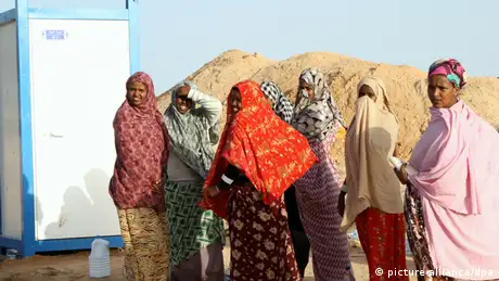 Somali women wearing colorful scarves queue outside a mobile toilet