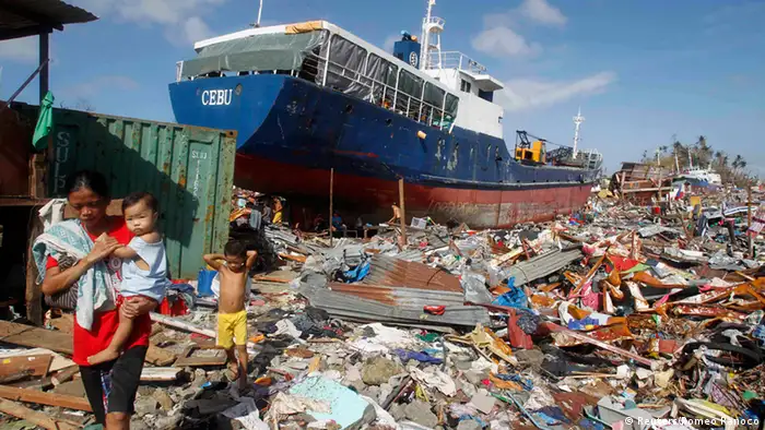 Residents walk past a cargo ship washed ashore four days after super typhoon Haiyan hit Anibong town, Tacloban city, central Philippines November 11, 2013. Dazed survivors of a super typhoon that swept through the central Philippines killing an estimated 10,000 people begged for help and scavenged for food, water and medicine on Monday, threatening to overwhelm military and rescue resources. REUTERS/Romeo Ranoco (PHILIPPINES - Tags: DISASTER MARITIME ENVIRONMENT)
