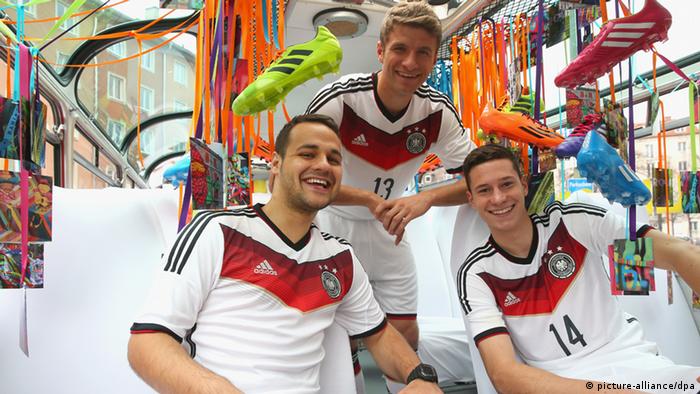 Die Nationalspieler Thomas Müller (2.v.r.) und Julian Draxler (r.) präsentieren neben Fußballfan Roman Wolf (l) bei einer Busfahrt in München das neue Trikot (Foto: Alexander Hassenstein/adidas/dpa)