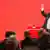 German politician Sigmar Gabriel raises his hand at a podium before a red backdrop. Photo: Hannibal