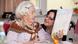 An elderly woman in bed looks at a sheet of paper held up in front of her by a carer An elderly woman in bed looks at a sheet of paper held up in front of her by a carer