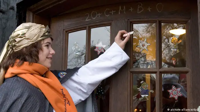 Ein Mädchen im Sternsingergewand schreibt den Segensspruch an die Haustür - Foto: picture alliance/dpa