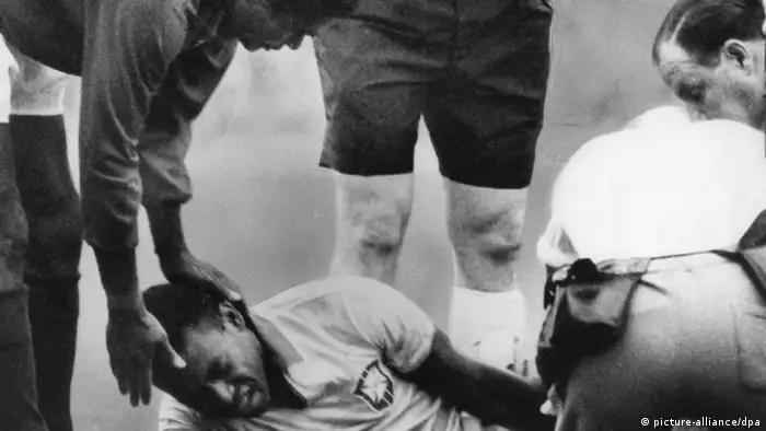 Brasiliens Stürmerstar Pele liegt am 19.7.1966 im Liverpooler Goodison Park mit schmerzverzerrtem Gesicht gefoult am Boden und wird von Betreuern behandelt; Portugals Stürmerstar Eusebio tröstet ihn (Foto: dpa)