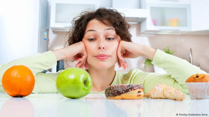 Una mujer mira una naranja, una manzana, una dona y un dulce de panadería.