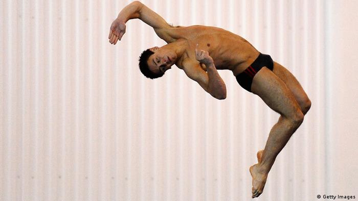 A man arcs his back as he dives backwards from a platform.