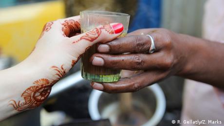 Bansi, a chai wallah near the Bombay High Court in Mumbai, Maharashtra hands a cup of chai to a tourist whose hands are decorated with mehndi.