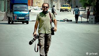 Bunyamin Aygun walks down an Aleppo street holding two cameras