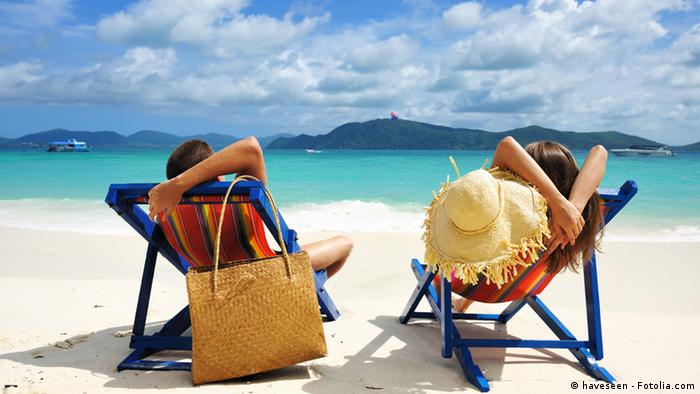 Couple sitting in lounge chairs on a tropical beach.
