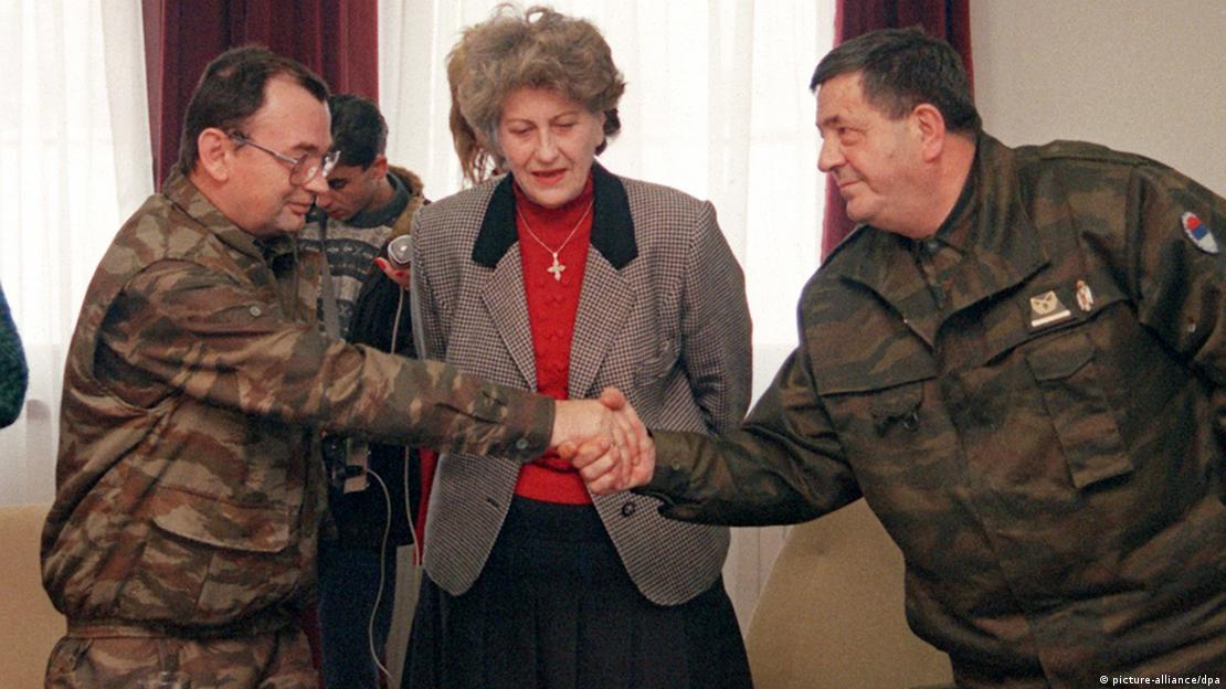 Biljana Plavšić u crvenoj rolci i sivom sakou u sredini, dok sa desne strane stoji Pero Čolić, a sa lijeve Manojlo Milanović. Obojica obučeni u maskirno vojničke uniforme