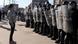 A protestor in Bosnia stands before a line of police officers holding shields. A protestor in Bosnia stands before a line of police officers holding shields.