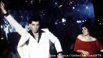John Travolta als Tony Manero tanzend auf der Tanzfläche einer Diskothek.