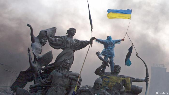 Манифестант размахивает флагом Украины, взобравшись на памятник