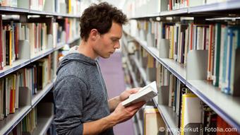 Ein Mann mit Buch in der Hand zwischen langen Bücherregalen