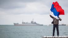 Ein Mann posiert am 16.03.2014 mit einer Russland-Fahne an der Bucht in Sewastopol, Ukraine. Im Hintergrund ein Schiff der russischen Schwarzmeerflotte. Mehr als 1,8 Millionen Krim-Bewohner aufgerufen, in einem Referendum über den Anschluss an Russland abzustimmen. Foto: Hannibal dpa +++(c) dpa - Bildfunk+++