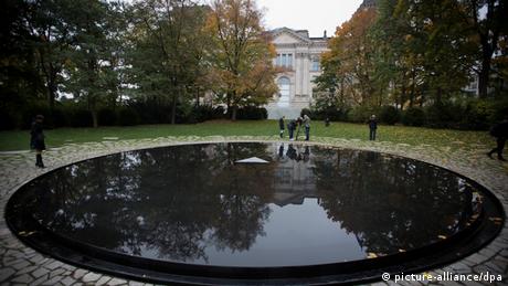 People walk next to the memorial's large reflecting pool in a park in Berlin.