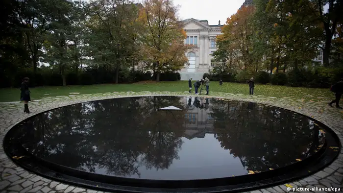 People walk next to the memorial's large reflecting pool in a park in Berlin.