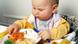 A baby sits at a high-chair eating from a plate of food A baby sits at a high-chair eating from a plate of food