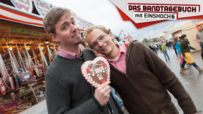 Zwei junge Männer in Trachtenmode halten ein Lebkuchenherz in die Kamera.