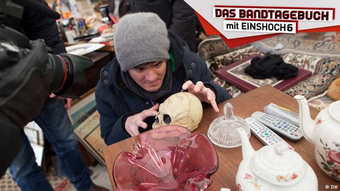 Tobi von der Band EINSHOCH6 betrachtet auf dem Flohmarkt mit grimmigem Blick einen Totenschädel aus Plastik