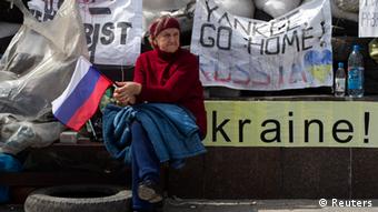 Eine Frau mit Russlandflagge in der Hand sitzt in Donezk vor Barrikaden und Plakaten mit Forderungen (Foto: REUTERS/Baz Ratner)