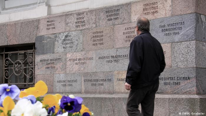 Цветы на фоне музея жертв геноцида в Вильнюсе, на стене которого таблички с фамилиями репрессированных