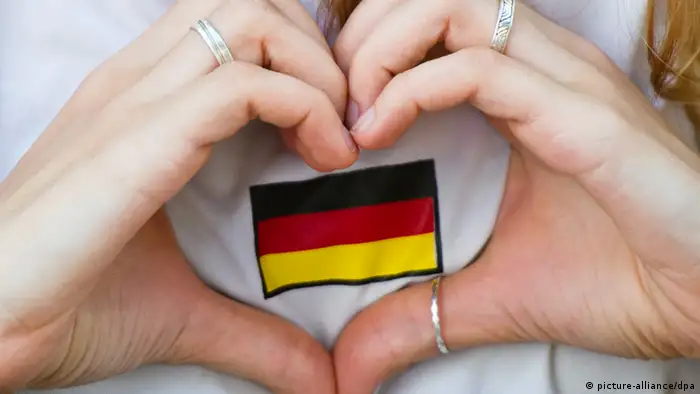 Zwei Hände formen ein Herz um eine kleine Deutschlandflagge auf einem T-Shirt