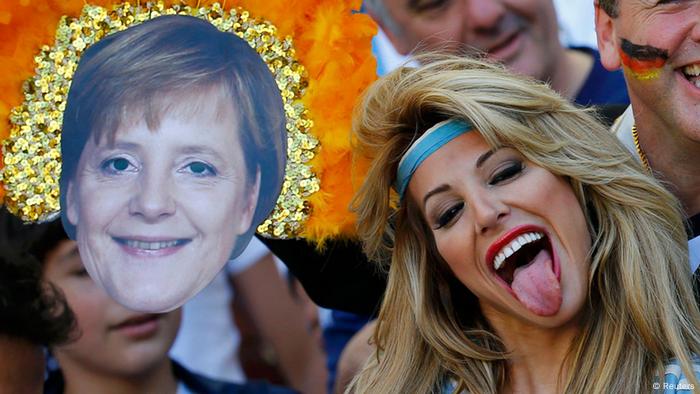 Eine Frau mit Stirnband streckt die Zunge heraus. Daneben ein Foto von Angela Merkels Kopf (Reuters)