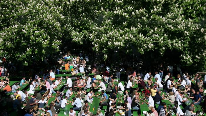 Menschen sitzen unter Kastanienbäumen in einem Biergarten