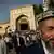 A Uighur man with a beard stands in front of a mosque in Xinjiang