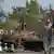 Жители города в Донецкой области на фоне сломанной военной машины