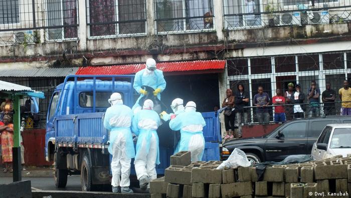 Local residents watch as a corpse is loaded on to a truck