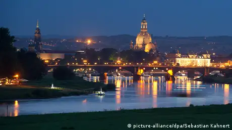 A view of Dresden at night fall acoss the river Elbe, reflecting the lights of the city and the illuminated dome of the Frauenkirche church.