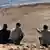 Four men sit on the ground in a desert setting