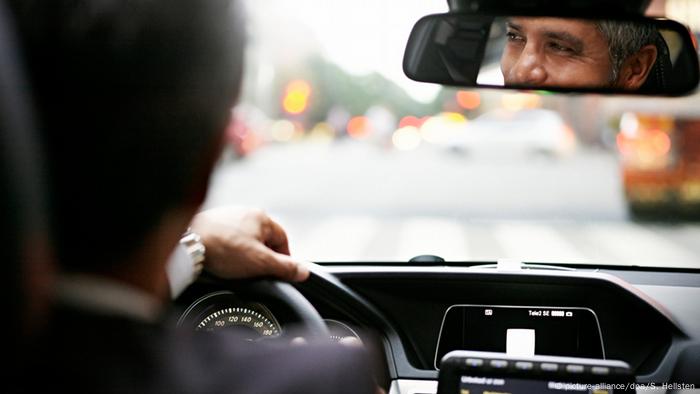 Un hombre sentado en un coche mirando por el espejo retrovisor.