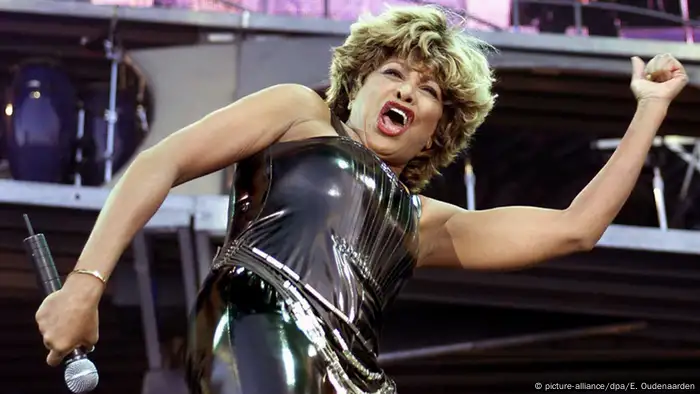 Tina Turner singing on stage in a black leather outfit
