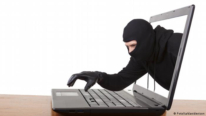 Symbolbild: Ein schwarz maskierter Mann mit schwarzen Handschuhen greift aus einem Laptop-Bildschirm auf die Tastatur (Foto: Fotolia/davidevison)