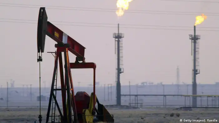 A derek pumps in a Kuwaiti oil field as a pair of gas flares burn in the background.