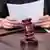 Foto simbólica de un mazo de juez con una persona al fondo que tiene papeles en la mano.