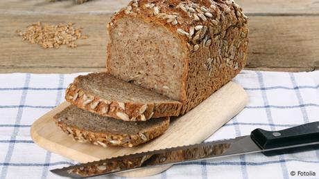 ein Vollkornbrot liegt auf einem Brettchen, daneben ein Brotmesser 