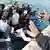 Ein Flüchtlingsboot wurde von der Marine gerettet und an Land gebracht. Während die Flüchtlinge an Land gehen wollen, machen Männer und Frauen mit ihren Händen eine abwehrende Geste. (Foto: picture-alliance/dpa/Ettore Ferrar)